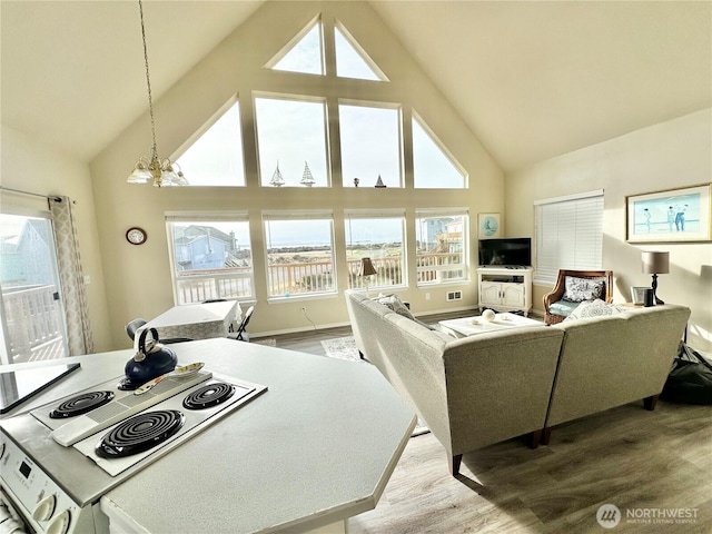 living area with high vaulted ceiling, baseboards, light wood finished floors, and a chandelier