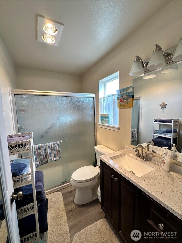 full bath with vanity, wood finished floors, a shower stall, and toilet