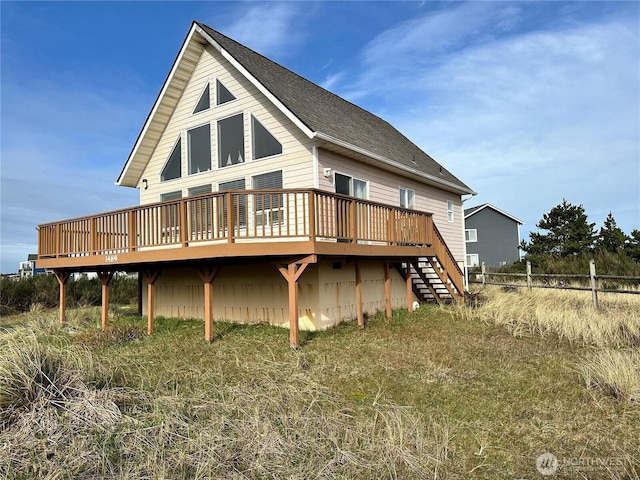 rear view of house featuring roof with shingles, a deck, stairs, and fence