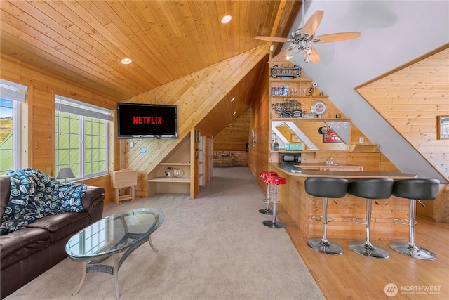 carpeted living area with vaulted ceiling, wooden walls, wood ceiling, and a dry bar