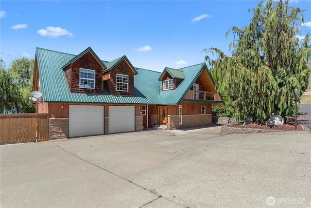 view of front of house with fence, stone siding, driveway, and metal roof