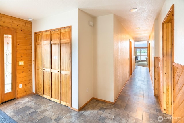 corridor with baseboards, a textured ceiling, stone tile flooring, and wood walls