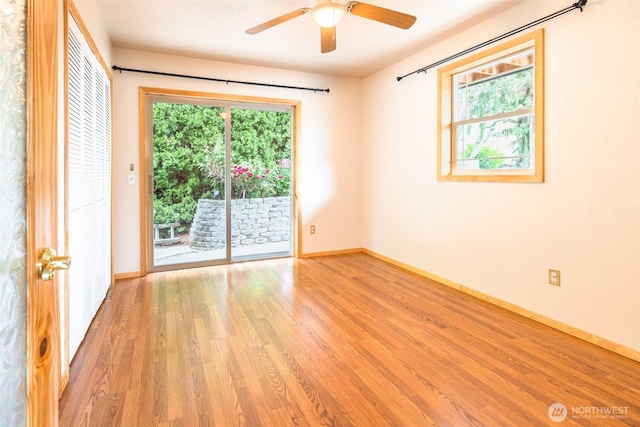 empty room with a wealth of natural light, baseboards, wood finished floors, and a ceiling fan