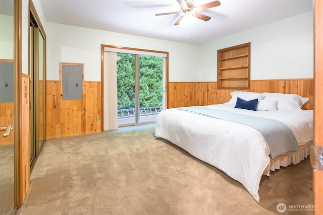 carpeted bedroom with a ceiling fan, electric panel, wood walls, wainscoting, and access to exterior