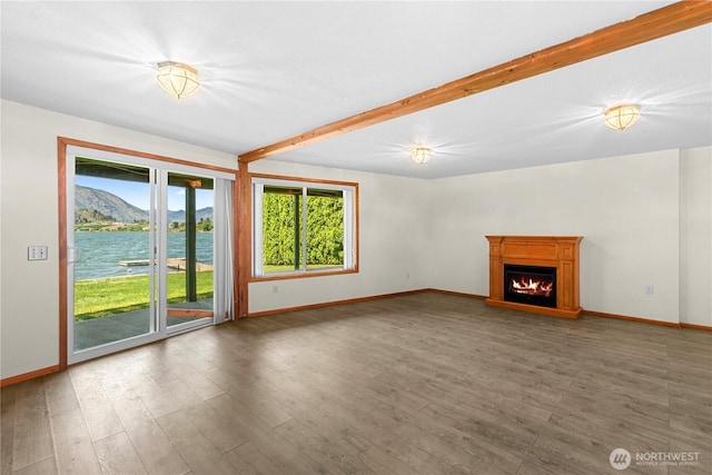 unfurnished living room featuring beam ceiling, a warm lit fireplace, wood finished floors, a mountain view, and baseboards