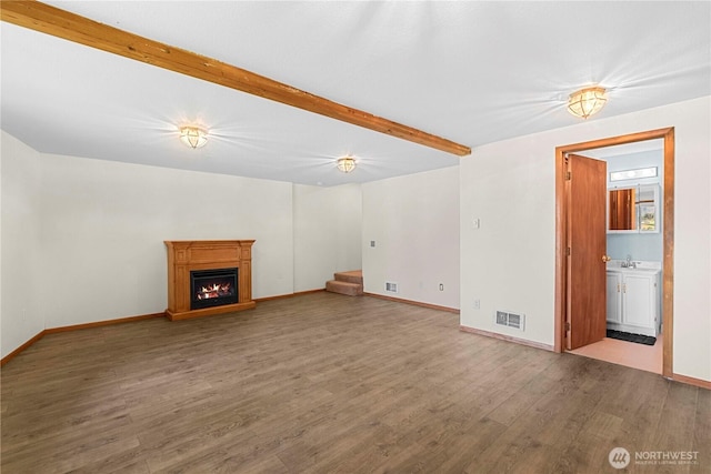 unfurnished living room featuring visible vents, beamed ceiling, stairway, a warm lit fireplace, and wood finished floors