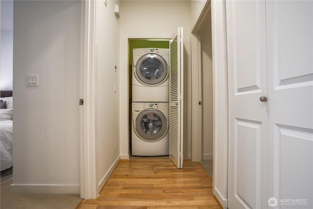 clothes washing area featuring laundry area, baseboards, stacked washer / drying machine, and light wood finished floors