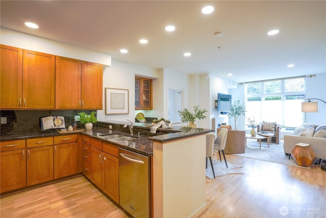 kitchen with backsplash, brown cabinets, light wood-style flooring, stainless steel dishwasher, and a sink