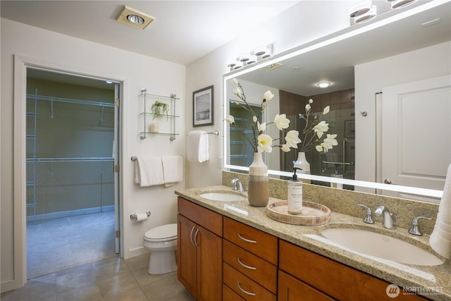 full bath featuring a sink, tiled shower, toilet, and double vanity