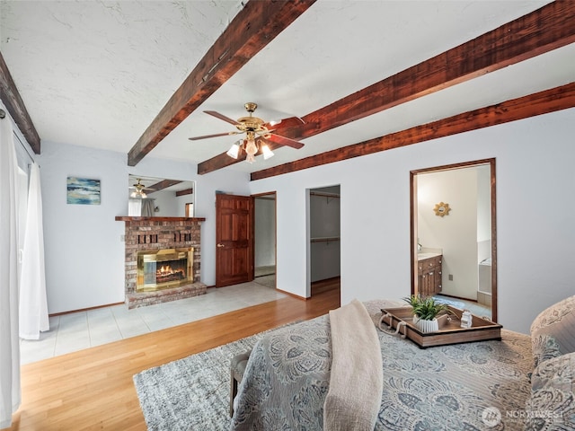 living room featuring beam ceiling, a ceiling fan, wood finished floors, baseboards, and a brick fireplace