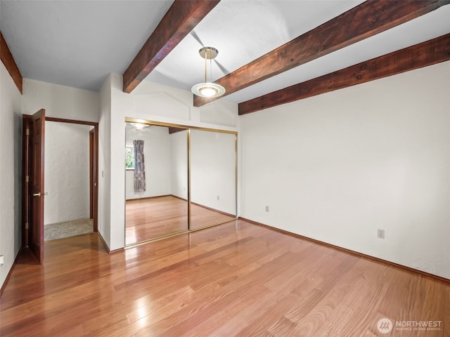 unfurnished bedroom with a closet, beamed ceiling, and wood finished floors