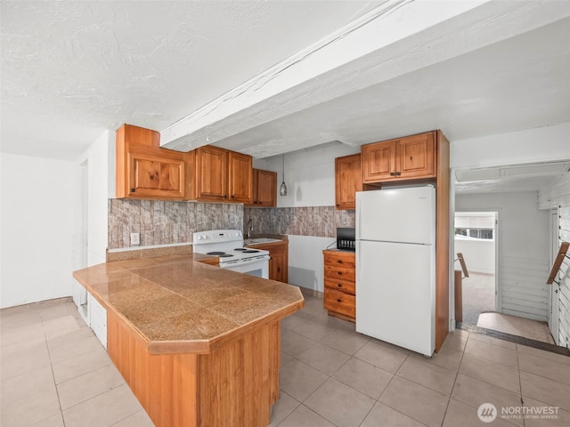 kitchen with tile counters, a peninsula, light tile patterned flooring, brown cabinetry, and white appliances