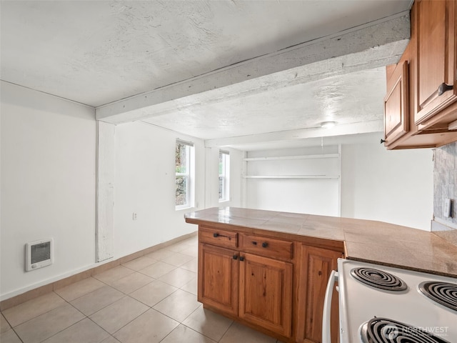 kitchen featuring electric range, heating unit, brown cabinetry, light tile patterned floors, and tile counters