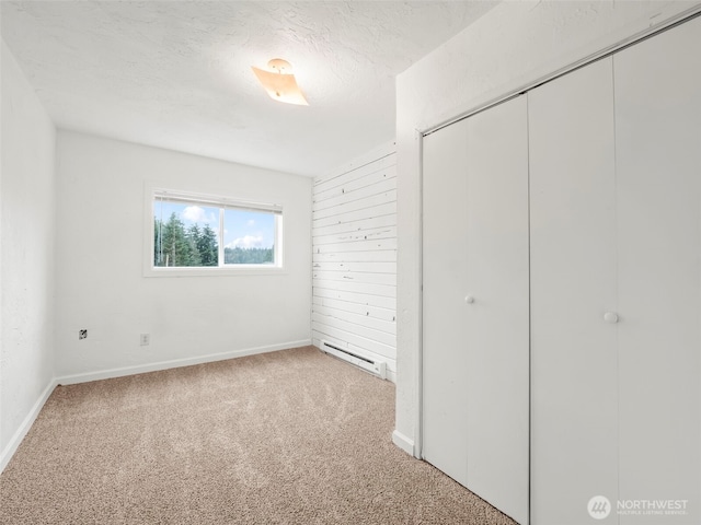 unfurnished bedroom featuring a baseboard heating unit, a textured ceiling, a closet, carpet, and baseboards