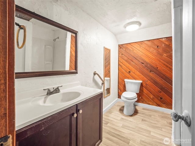 full bathroom featuring toilet, wood finished floors, wood walls, vanity, and a textured wall