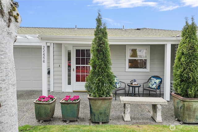 doorway to property featuring an attached garage and roof with shingles