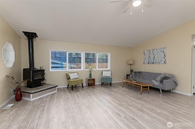 sitting room featuring light wood-type flooring, visible vents, a ceiling fan, a wood stove, and vaulted ceiling