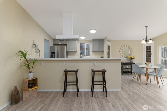 kitchen with an inviting chandelier, gray cabinets, light countertops, a kitchen bar, and stainless steel fridge