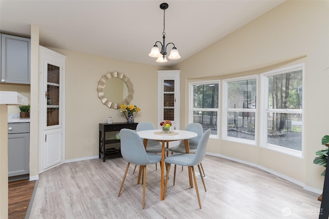 dining area with a chandelier, light wood finished floors, baseboards, and lofted ceiling