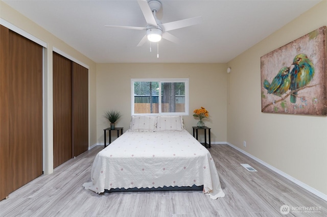 bedroom with visible vents, two closets, baseboards, ceiling fan, and light wood-style flooring