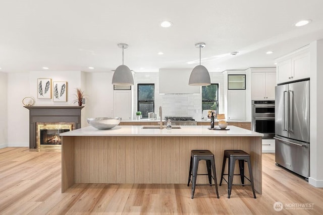 kitchen featuring a sink, stainless steel appliances, light countertops, light wood-style floors, and backsplash