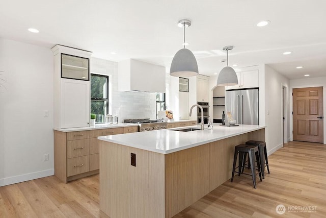 kitchen with a sink, backsplash, wall chimney exhaust hood, light wood finished floors, and high end refrigerator