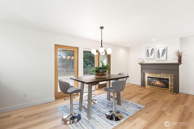 dining room featuring a fireplace with flush hearth, baseboards, and light wood finished floors