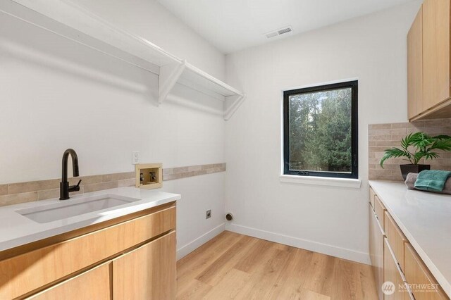 washroom with visible vents, washer hookup, light wood-style flooring, a sink, and baseboards