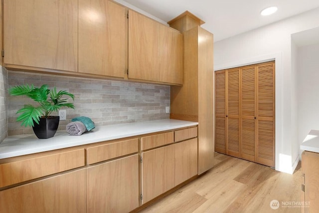 kitchen with light brown cabinets, light countertops, light wood-type flooring, decorative backsplash, and recessed lighting