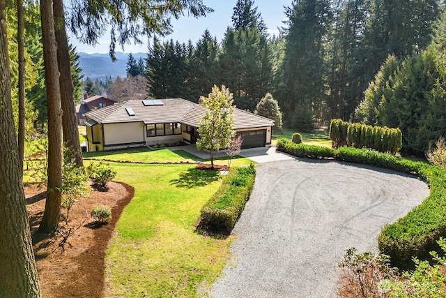 view of front of house with driveway, roof mounted solar panels, a mountain view, an attached garage, and a front yard