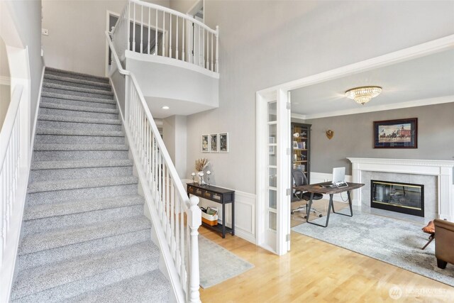 stairs featuring a high end fireplace, ornamental molding, wainscoting, a high ceiling, and wood finished floors