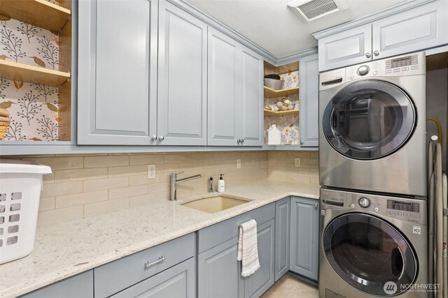 laundry room featuring stacked washer and dryer, cabinet space, visible vents, and a sink