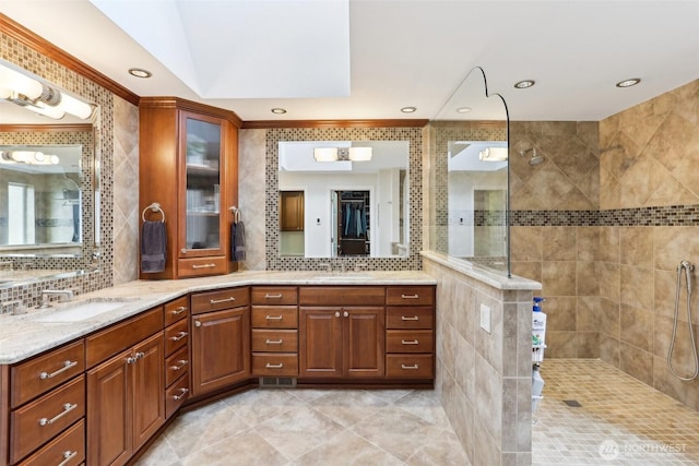 bathroom featuring double vanity, backsplash, walk in shower, and a sink