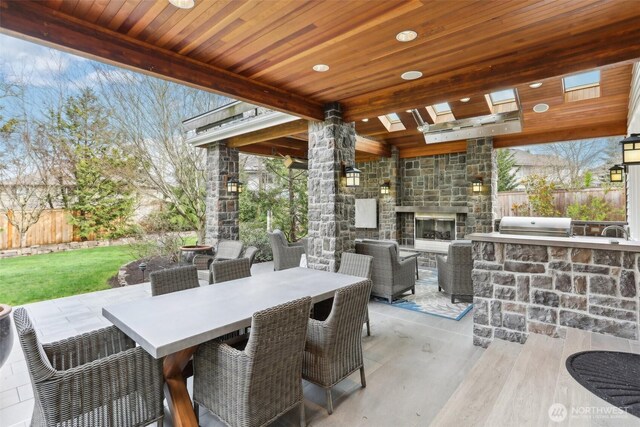 view of patio featuring outdoor dining space, fence, grilling area, an outdoor stone fireplace, and exterior kitchen