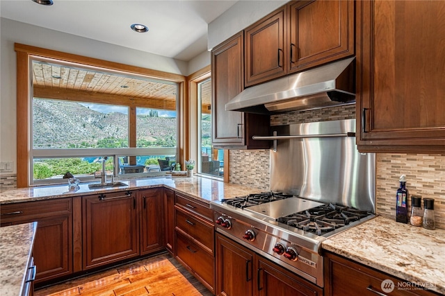 kitchen with tasteful backsplash, under cabinet range hood, stainless steel gas stovetop, and light stone counters