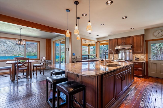 kitchen with a sink, dark wood-style floors, under cabinet range hood, decorative backsplash, and light stone counters