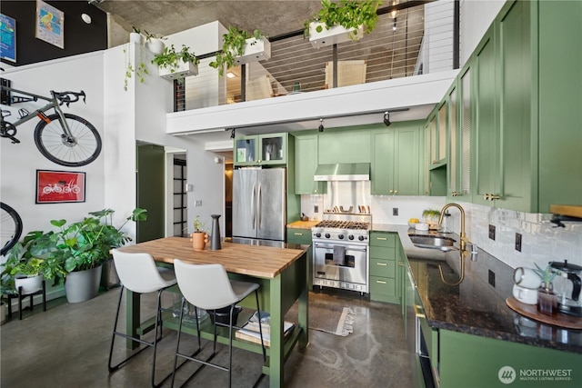 kitchen with a sink, appliances with stainless steel finishes, wall chimney exhaust hood, and green cabinetry