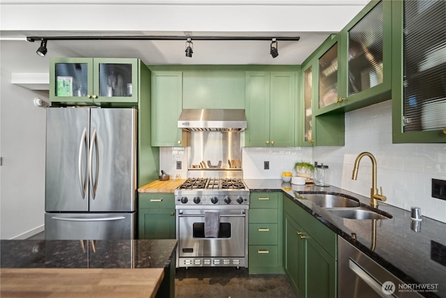 kitchen with a sink, stainless steel appliances, green cabinets, and wall chimney range hood