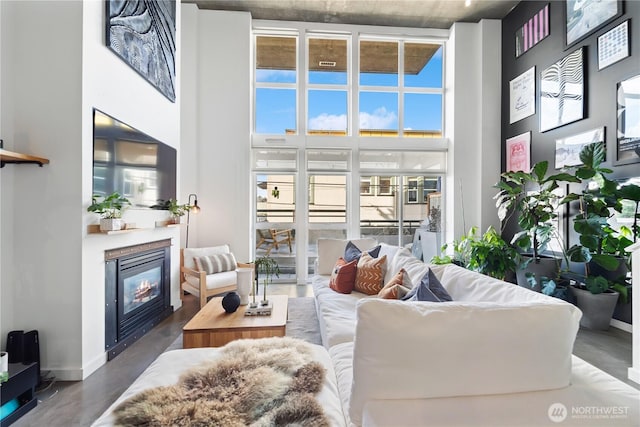 living area featuring expansive windows, baseboards, a high ceiling, and a glass covered fireplace