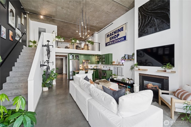 living room featuring a glass covered fireplace, stairway, concrete flooring, and a towering ceiling