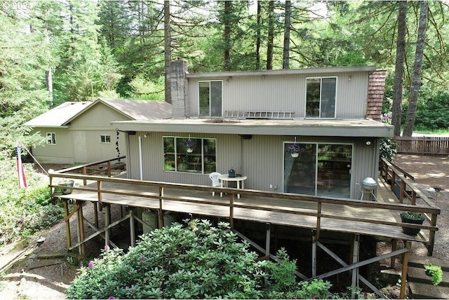 rear view of property featuring a wooden deck, a view of trees, a chimney, and fence