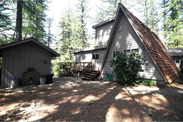 rear view of property featuring a wooden deck, board and batten siding, an outdoor structure, and a shed