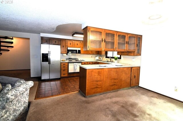 kitchen with glass insert cabinets, light countertops, a peninsula, stainless steel appliances, and a sink