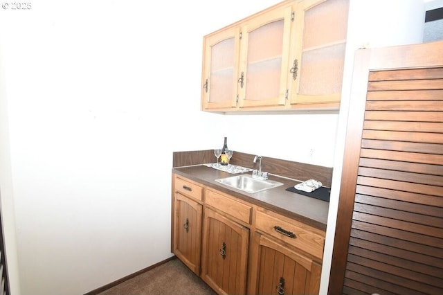 kitchen featuring dark countertops, baseboards, dark colored carpet, and a sink