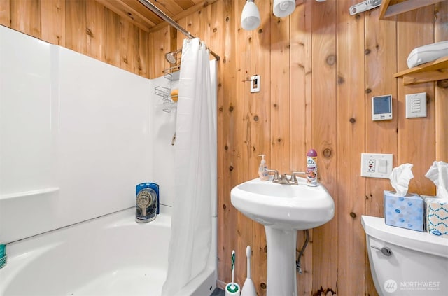 bathroom featuring a sink, curtained shower, toilet, and wood walls