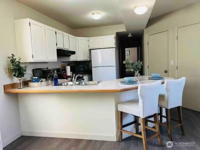 kitchen featuring under cabinet range hood, a sink, white cabinetry, freestanding refrigerator, and a peninsula