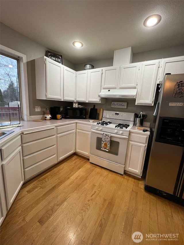 kitchen with black microwave, under cabinet range hood, white gas range oven, light wood-style floors, and stainless steel fridge