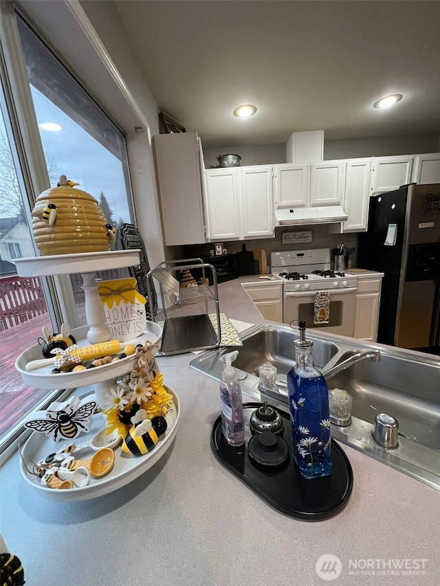 kitchen with white range with gas stovetop, stainless steel fridge with ice dispenser, light countertops, white cabinets, and under cabinet range hood