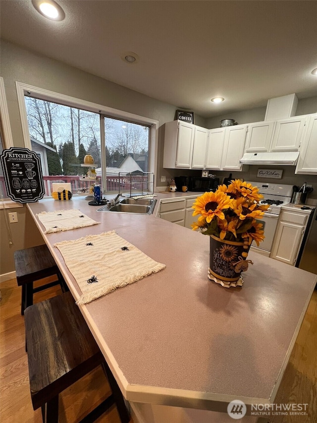 kitchen with a peninsula, light wood-style flooring, white range with gas stovetop, recessed lighting, and white cabinetry