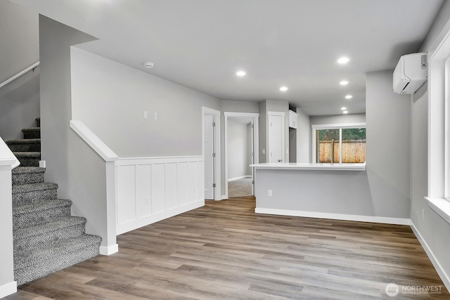 spare room with a wall mounted air conditioner, wood finished floors, recessed lighting, baseboards, and stairs